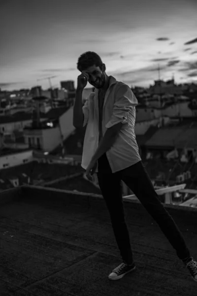 Eşcinsel çocuk beyaz bir tişörtle çatıda poz veriyor düğmeleri açık ve anın tadını çıkarıyor.