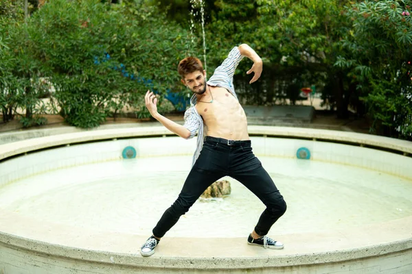 Madrid sokaklarında ağaçlarla çevrili beyaz bir çeşmede akrobatlık yapan genç bir çocuk.