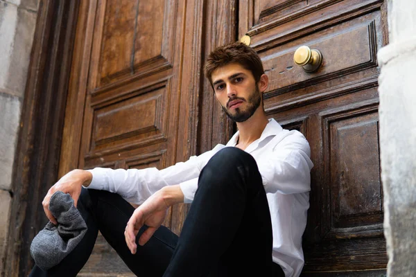 Masum bakışları olan genç bir çocuk eski bir kapının önünde oturuyor.