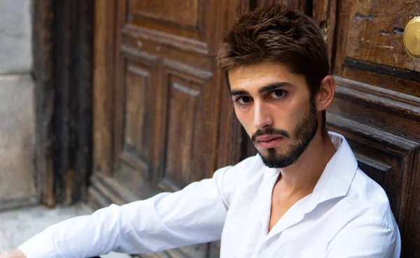 Masum bakışları olan genç bir çocuk eski bir kapının önünde oturuyor.