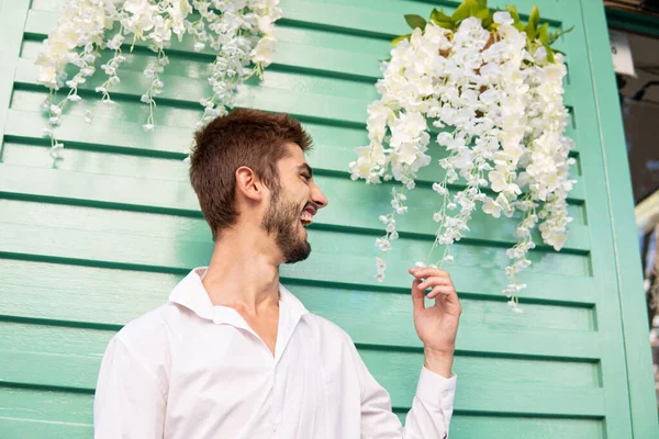 Beyaz gömlekli ve beyaz çiçekli genç bir çocuk, bir turkuaz demirin önünde.