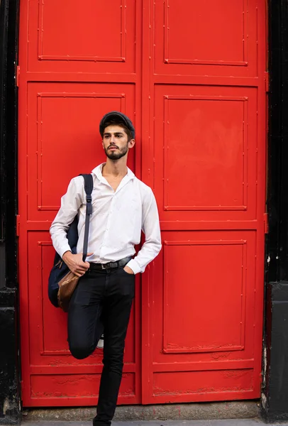 Kırmızı kapının önünde bereli ve sırt çantalı genç bir çocuk.