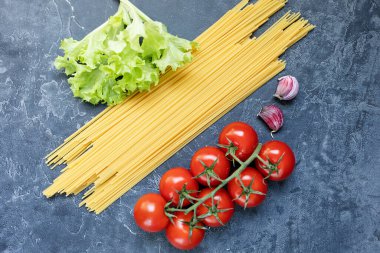 Buğday ve olgun vişneli domateslerden yapılmış spagetti bir dalda, sarımsak ve baharatlarla. Koyu grafit arkaplanda taze yeşiller. Lezzetli makarna yapmak için ürünler. Yukarıdan görünüşü.