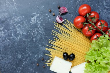 Buğday ve olgun vişneli domateslerden yapılmış spagetti bir dalda, sarımsak ve baharatlarla. Koyu grafit arkaplanda taze yeşiller. Lezzetli makarna yapmak için ürünler. Yukarıdan görünüşü.