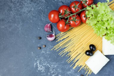 Buğday ve olgun vişneli domateslerden yapılmış spagetti bir dalda, sarımsak ve baharatlarla. Koyu grafit arkaplanda taze yeşiller. Lezzetli makarna yapmak için ürünler. Yukarıdan görünüşü.