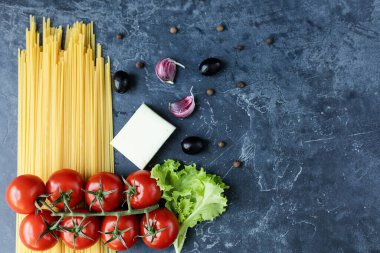 Buğday ve olgun vişneli domateslerden yapılmış spagetti bir dalda, sarımsak ve baharatlarla. Koyu grafit arkaplanda taze yeşiller. Lezzetli makarna yapmak için ürünler. Yukarıdan görünüşü.