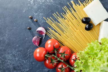 Buğday ve olgun vişneli domateslerden yapılmış spagetti bir dalda, sarımsak ve baharatlarla. Koyu grafit arkaplanda taze yeşiller. Lezzetli makarna yapmak için ürünler. Yukarıdan görünüşü.