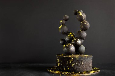 Siyah arka planda çikolata topları ve parlak sarı lekeler olan siyah, vahşi bir pasta. Tatil konsepti ve dünya pasta günü. seçici odak.