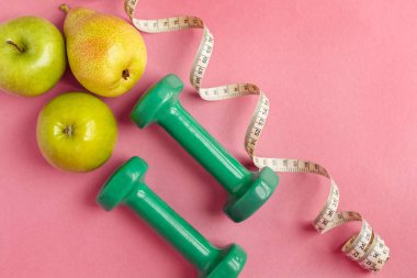 Dambılı kompozisyon, bükülmüş mezura ve pembe arka planda yeşil elma, üst manzara. Diyet ve sağlıklı yaşam tarzı kavramı