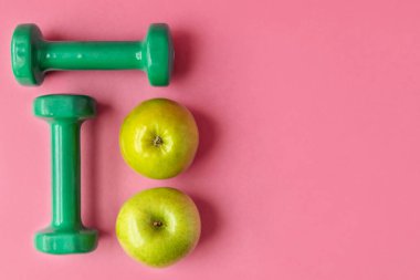 Halterli kompozisyon ve pembe arka planda yeşil elmalar, üst manzara. Beslenme ve sağlıklı yaşam tarzı kavramı. Boşluğu kopyala.