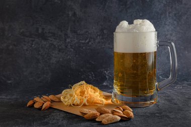 Cam bardakta köpüklü hafif bira, koyu arkaplanda Cecil peyniri ve badem. Soğuk kehribar içeceği kavramı.