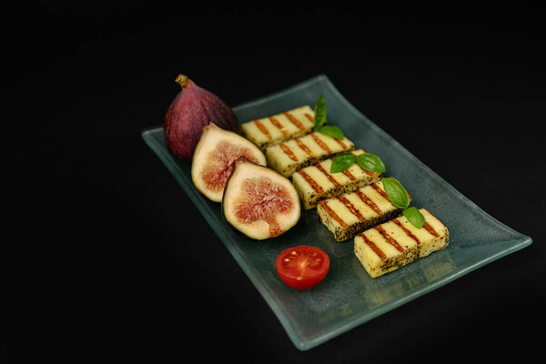 Жареные ломтики сыра галлуми на тарелке с инжиром и листьями базилика на тёмном фоне. Традиционный сыр Греции и Турции. скопировать пространство. Плоская постель.