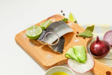 Baharatlı tuzlu ringa balığı kompozisyonu, limon dilimleri ve kırmızı soğan halkaları beyaz bir masada tahta kesme tahtasında..