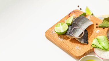 Baharatlı tuzlu ringa balığı kompozisyonu, limon dilimleri ve kırmızı soğan halkaları beyaz bir masada tahta kesme tahtasında..