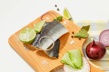 Baharatlı tuzlu ringa balığı kompozisyonu, limon dilimleri ve kırmızı soğan halkaları beyaz bir masada tahta kesme tahtasında..