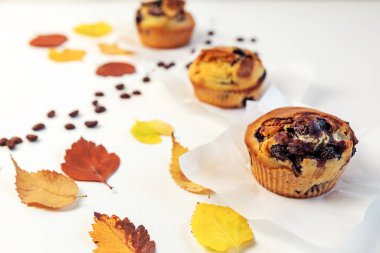 Lezzetli yaban mersinli kekler, parlak sonbahar yaprakları ve beyaz bir masada kahve çekirdekleri. seçici odak.