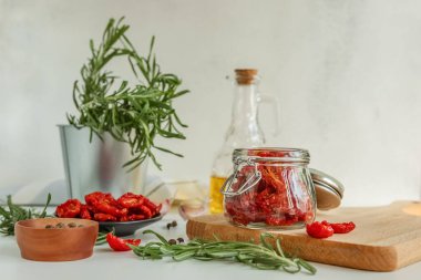 Ev yapımı kurutulmuş domatesler, cam şişede zeytinyağı, taze biberiye ve arka planda baharatlar. Mutfak için parmak izi. seçici odak.