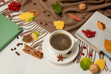 Sonbahar kompozisyonu. Bardakta kahve, kahverengi eşarp, kitap, tarçın çubukları, beyaz bir masanın üzerine düşen yapraklar. Seçici odak.