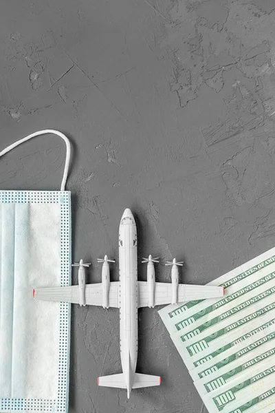 a toy plane on a gray concrete background, dollar bills, and a face mask, the concept of closing borders around the world due to coronavirus, financial losses of airlines and tour operators.