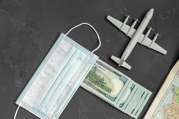 a toy plane on a gray concrete background, dollar bills, a face mask, the concept of closing borders around the world due to coronavirus, financial losses of airlines and tour operators.