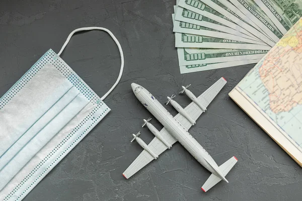 a toy plane on a gray concrete background, dollar bills, a face mask, the concept of closing borders around the world due to coronavirus, financial losses of airlines and tour operators.