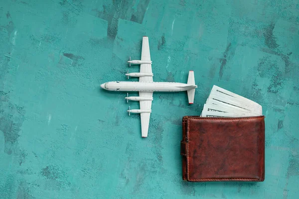 a toy plane on a green concrete background, a man\'s wallet with dollar bills, the concept of closing borders around the world due to coronavirus, financial losses of airlines and tour operators.