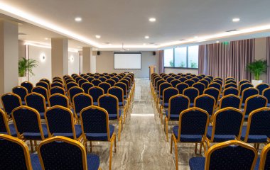 Boş beyaz ekranlı lüks oditoryum manzarası. Klasik mavi ve altın koltuklu modern konferans salonu