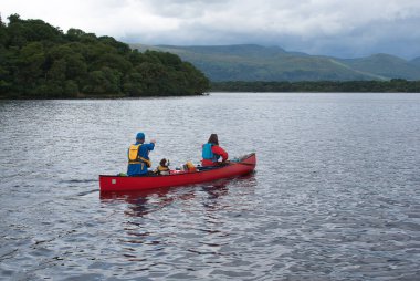 Two people and a dog canoeing in Loch Lomond, Scotland. clipart