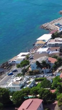 Huzurlu Mavi Deniz boyunca Rocky Shoreline ve Renkli Binalarla Sahra Manzarası