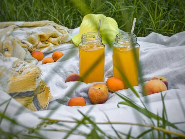 Relaxing on a nature, park, garden, countryside. Background with fruits, hat, two glass jars with straws pineapple-orange juice on the grass. Blur, fuzzy background. Natural food, healthy lifestyle.