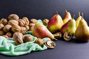 Sulu, taze kırmızı-sarı armutlar, açık yeşil bir beze serilmiş cevizler, siyah arka plan..