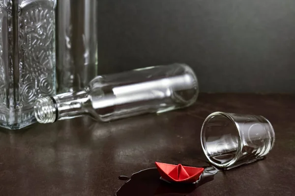 ボトルを背景に古い木製のテーブルの上にこぼれたアルゴールと紙の赤いボート 折り紙とガラスのスタック 暗い背景 健康的なライフスタイル アルコール依存症中毒 — ストック写真