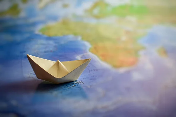 White paper boat on the world map. Origami. Traveling around the world.