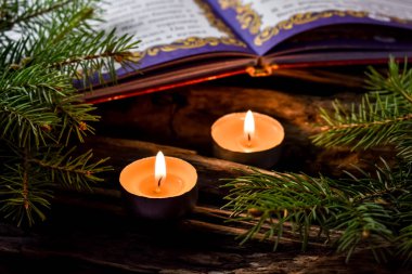  İki yanan mum, köknar dalları ve tahta arka planda açık bir kitabı olan kompozisyon. Evde Yeni Yıl ve Noel kutlamaları konsepti.