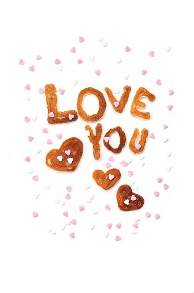Food typography phrase Love You performed from Alphabet Pancakes with sprinkles. Lettering Isolated on white background. Top view, close up