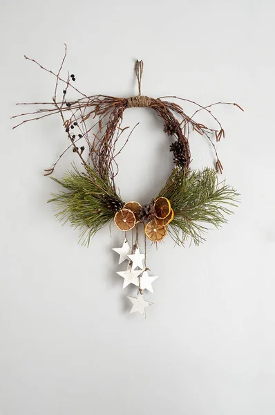 Rustic Christmas wreath with dried orange slices, pine cones and birch twigs. Frontal view on a gray concrete wall with copy space