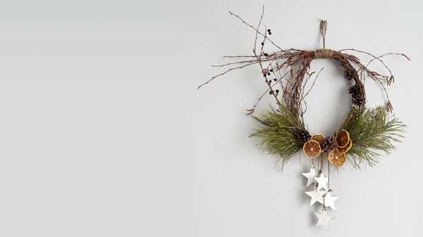 Rustic Christmas wreath with dried orange slices, pine cones and birch twigs. Frontal view on a gray concrete wall with copy space