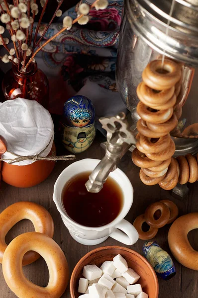 Traditional Russian Tea Party including hot black tea from samovar, lump sugar, crunch bagels sushki and baranki. Decoration with russian doll Matryoshka on wooden background