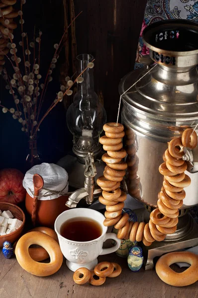Traditional Russian Tea Party including hot black tea from samovar, lump sugar, crunch bagels sushki and baranki. Decoration with russian doll Matryoshka on wooden background