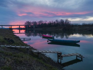 Renkli bir günbatımında, bulutlu bir günde, nehir kıyısı boyunca kıyıya demirlemiş teknelerin güzel manzarası..
