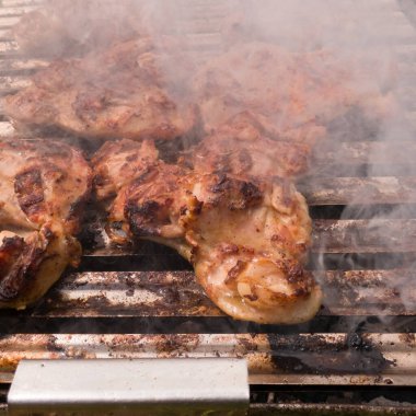 Gün boyunca ızgarada kızarırken etrafları dumanla çevrili kemiksiz tavuk budu yakın plan görüntüsü. Barbeküde tavuk eti (barbekü). Yemek hazırlama konsepti.