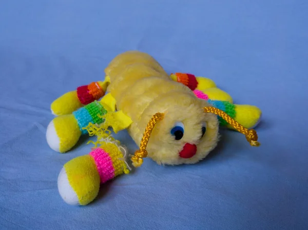 Mavi dokuya karşı izole edilmiş çocuk oyuncağı, çocukluktan kalma oyuncak ayı, yırtık sarı bir kırkayak.