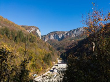 Güneşli bir günde, sonbaharda binanın üstündeki ormanla kaplı sarp kayalık bir dağın manzarası.