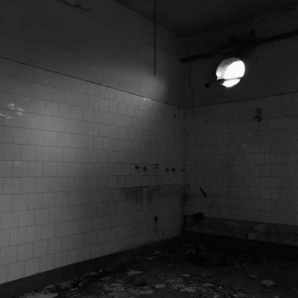 Abandoned messy empty room with wall tiles and a round opening in the wall.