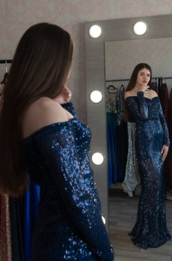 Balo için kıyafetini seçen çekici genç bir kadın. Aynanın önünde duran kadın. Aynaya odaklan. Balo, düğün ya da fotoshot için kiracı dükkanındaki lüks elbise..