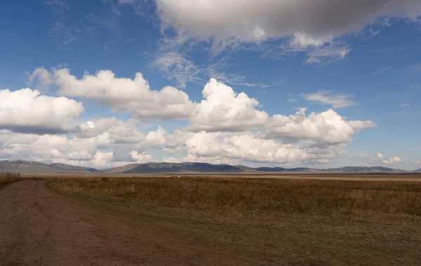 D'énormes nuages blancs près du sol dans la steppe de Khakassia. Paysage avec un large chemin de terre allant dans la steppe. Images De Stock Libres De Droits