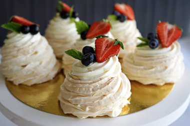   Beyaz krema ve taze böğürtlenlerle süslenmiş Pavlova kekleri altın bir tabakta beyaz bir tabakta yatıyor.                               