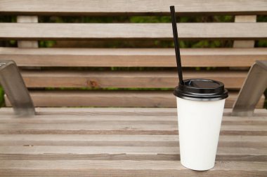 Siyah kapaklı beyaz bir kahve fincanı ve tahta bir bankta duran siyah bir tüp..