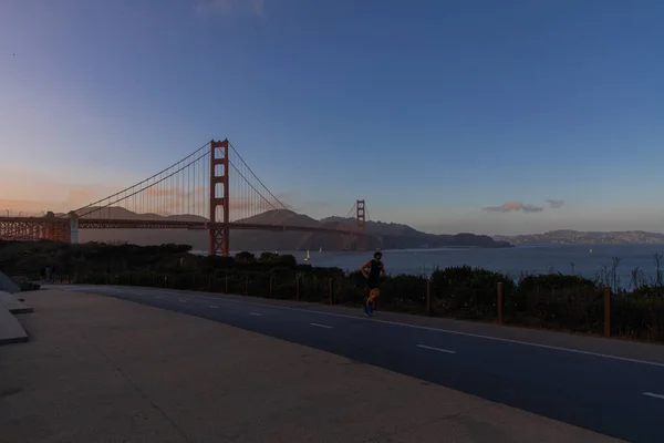 男は夕方の夕日の後ろにゴールデンゲートブリッジで実行されます サンフランシスコのバッテリービスタポイントからの眺め — ストック写真