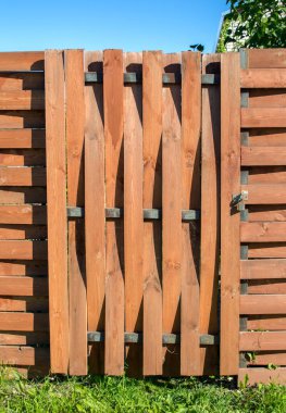 Tahta kavisli tahtalardan yapılmış, kahverengi çitli kilitli bir kapı. gri metal kilit